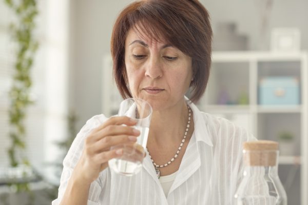Suspicious middle age woman looking glass of water Suspicious middle age woman looking glass of water